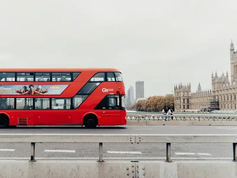 red bus on a bridge with historic buildings in the background