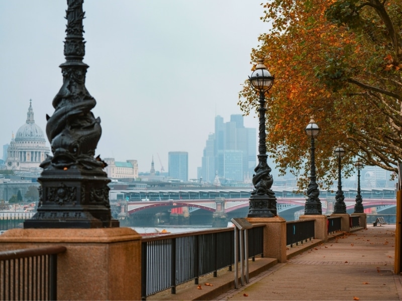 Urban river bank with ornate black lamp posts and a view across the river of a domed church and modern skyscrapers
