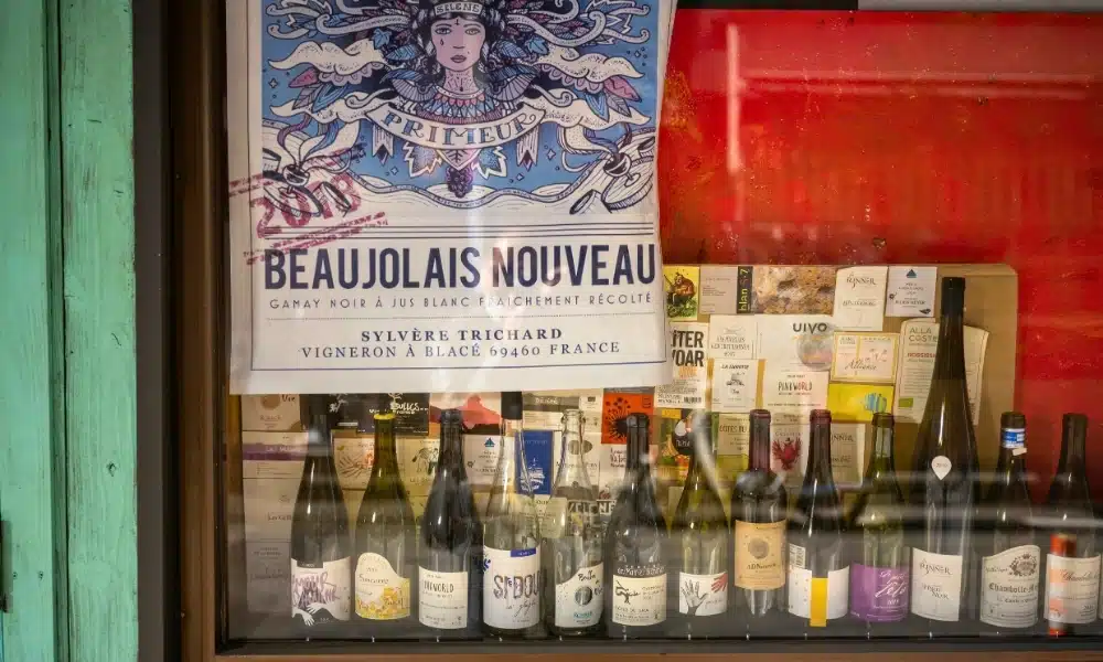 Bottles of red wine in a shop window with a poaster above advertising Beaujloais Nouveau