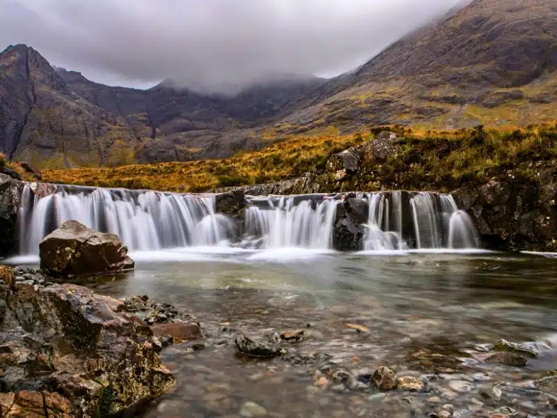 small and wide wtarefall over black rocks and surrouned by autumn bracken