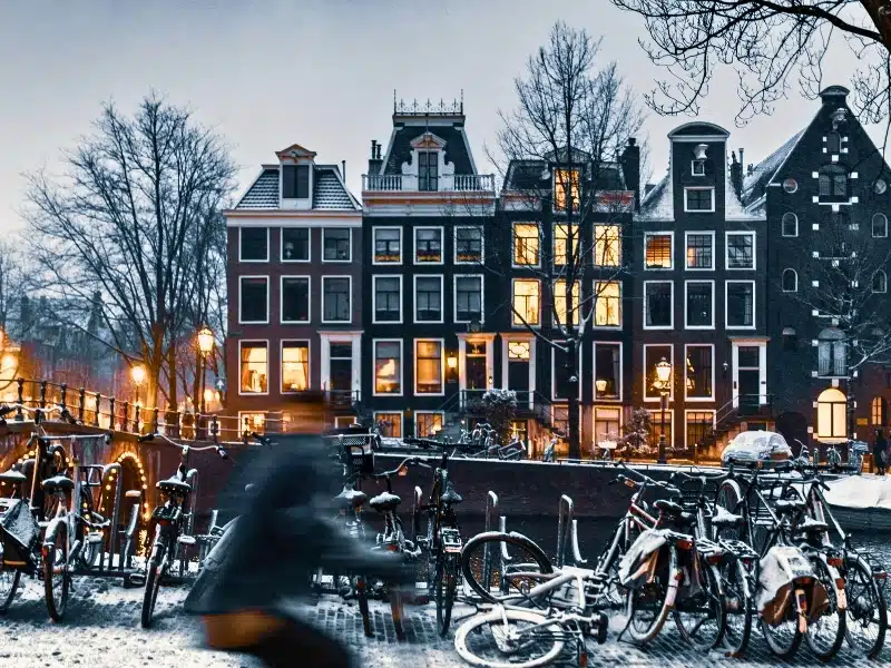 Dark painted canal houses in the evening facing a stand of bikes with. alight dusting of snow