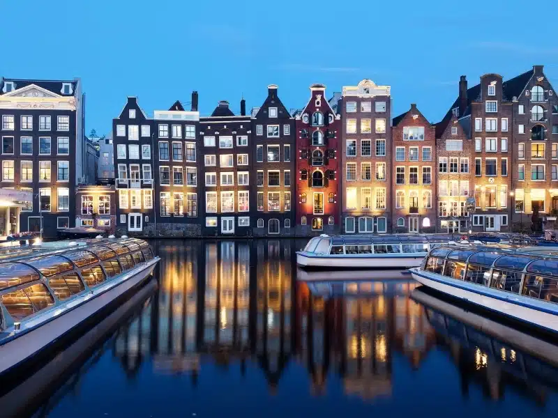 Glass topped canal boats moored on a stretch of water backed by tall and narrow Dutch town houses
