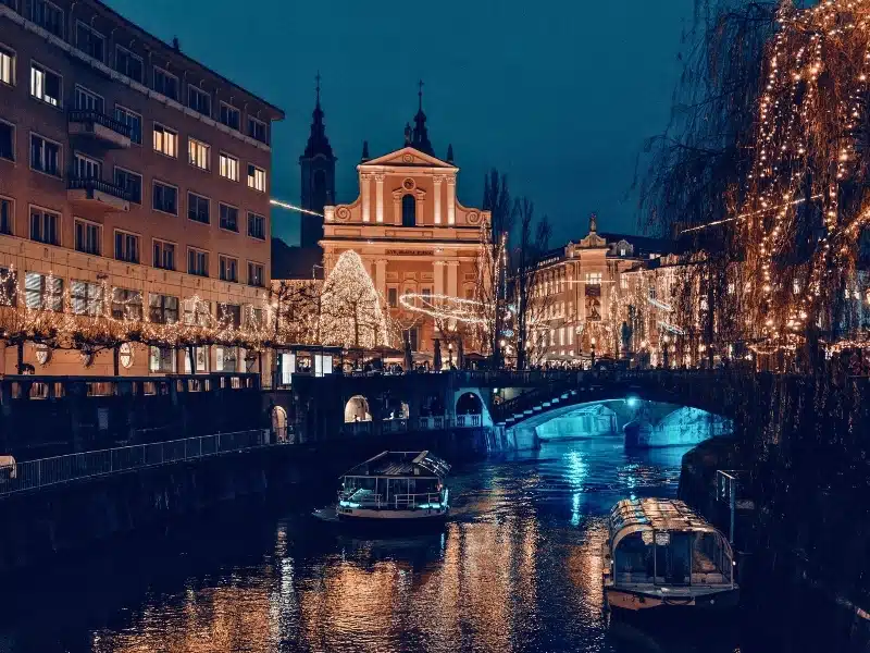 A city canal with glass topped river boats lit up and decorated for Christmas