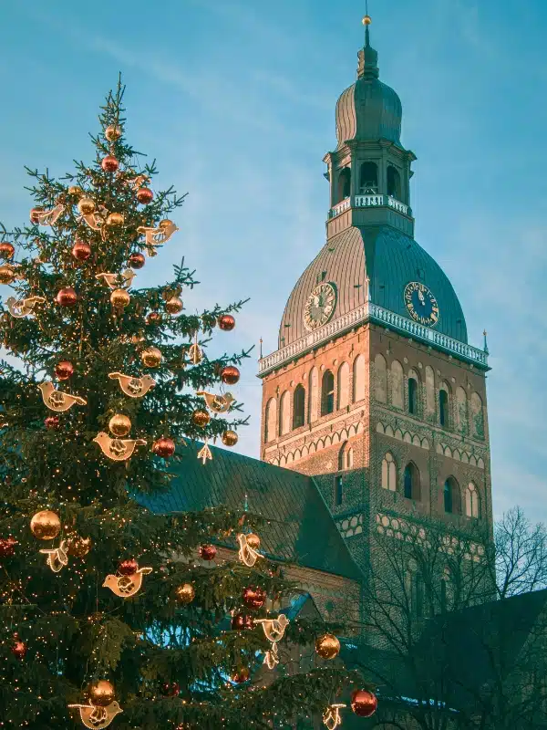 A Christmas tree decorated with gold baubles and doves sits in front of a Romanesque designed cathedral with a clock tower