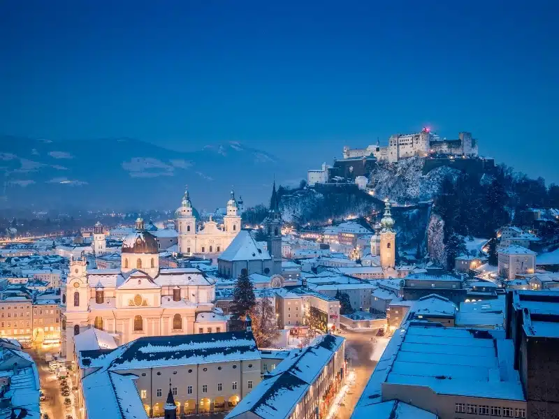 A snowy Austrian city with a castle on a nearby hill