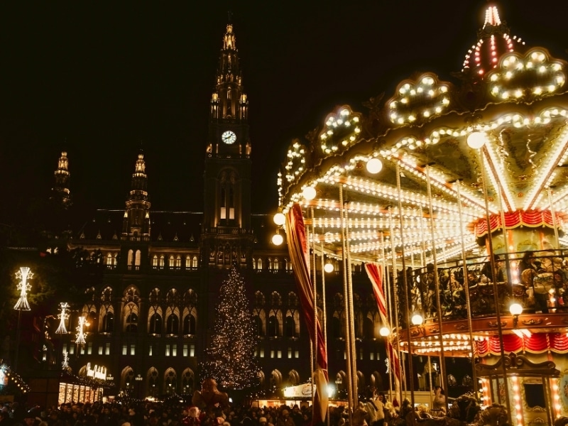 Traditional merry-go-round carousel in the centre of a busy Christmas Market backed by a historic building