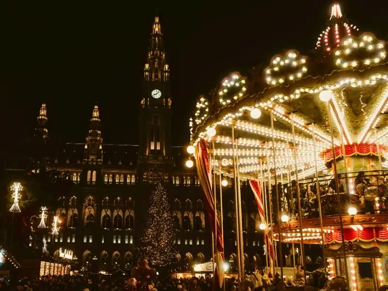 Traditional merry-go-round carousel in the centre of a busy Christmas Market backed by a historic building