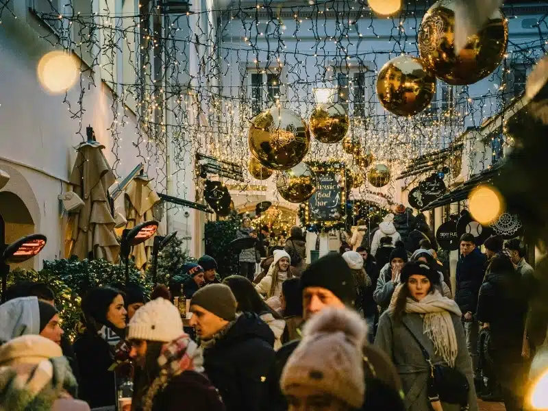 Busy city alley strung with lights and gold Christmas baubles as people drink under heat lamps and walk by the shops