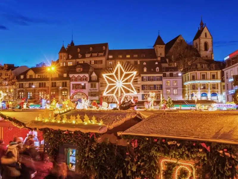 Large glowing star tops Christmas market stalls in front of a row of historic buildings and a church