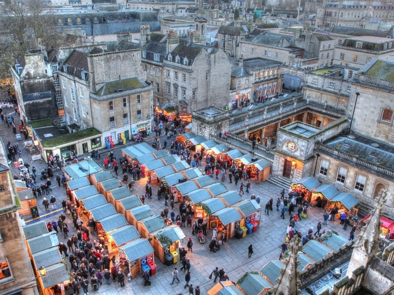 Small wooden huts of a Christmas market surrouned by historic stone buildings