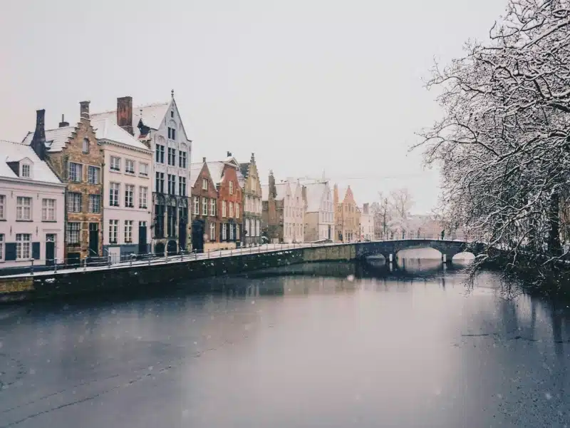 A snowy and icy canal with traditional Dutch canal houses facing bare trees over the water
