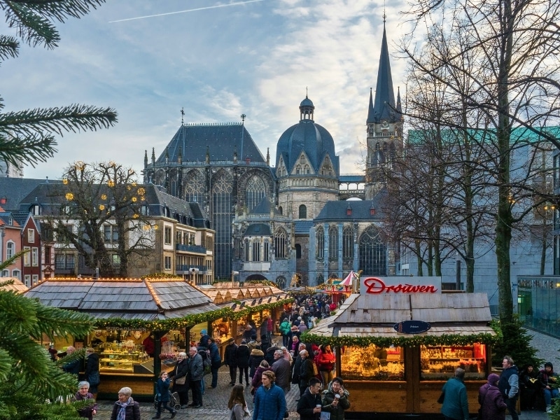 people walkign through. aChristmas Market with an imposing cathedral in the background with both spire and dome