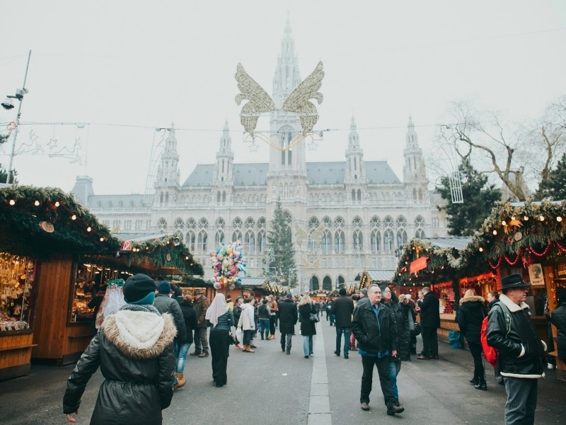 Decorated Chrstmas market stalls line a square in front of an elegent building with many spires
