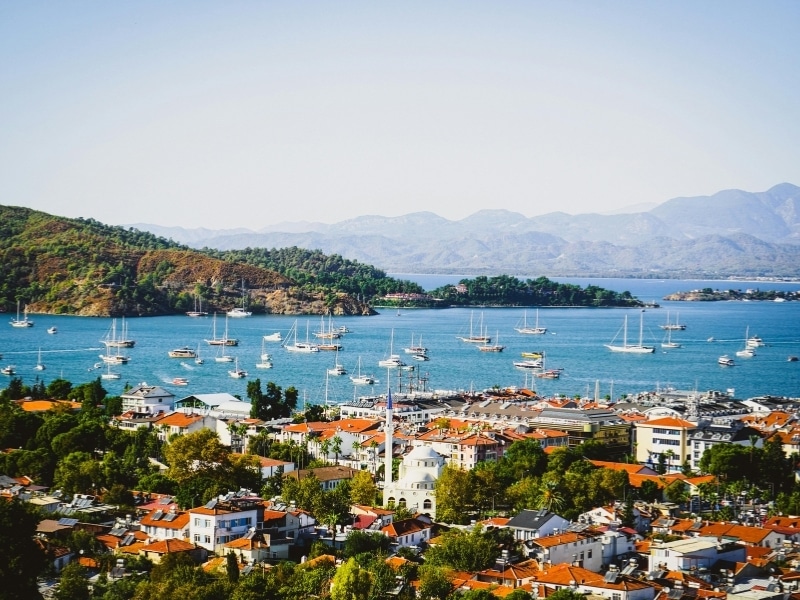 Busy harbor of a town with white buildiings and red roofs with wooded islands in the distance