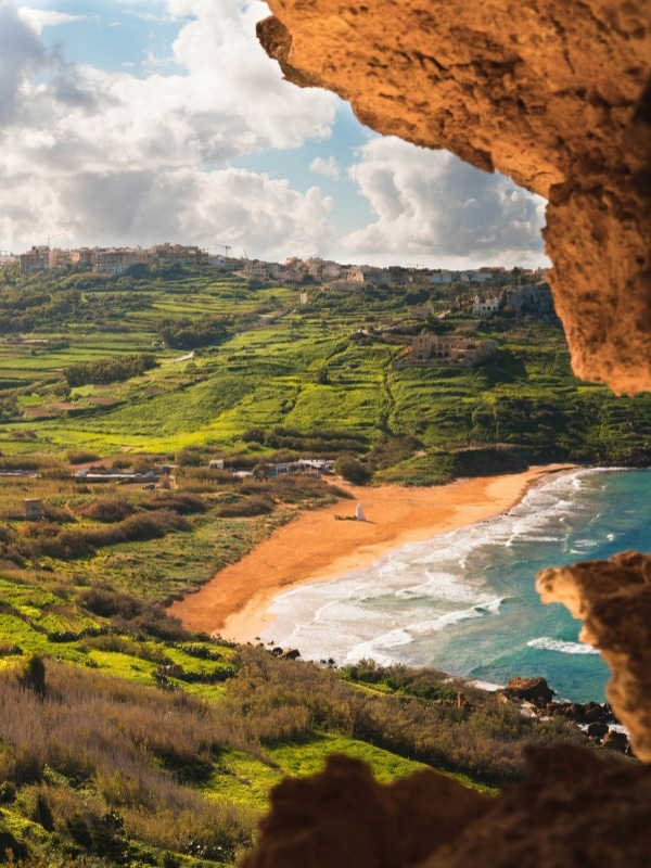 View of an empty beach surrounded by rolling grassy hills seen from a rocky cliff