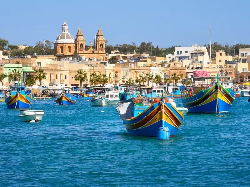 Harbor full of brighly painted boats against a backdrop of historical buildings and a domed church