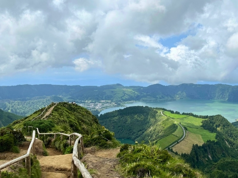 path with wooden handrailswith a view of lush fields and woods to a turquoise bay