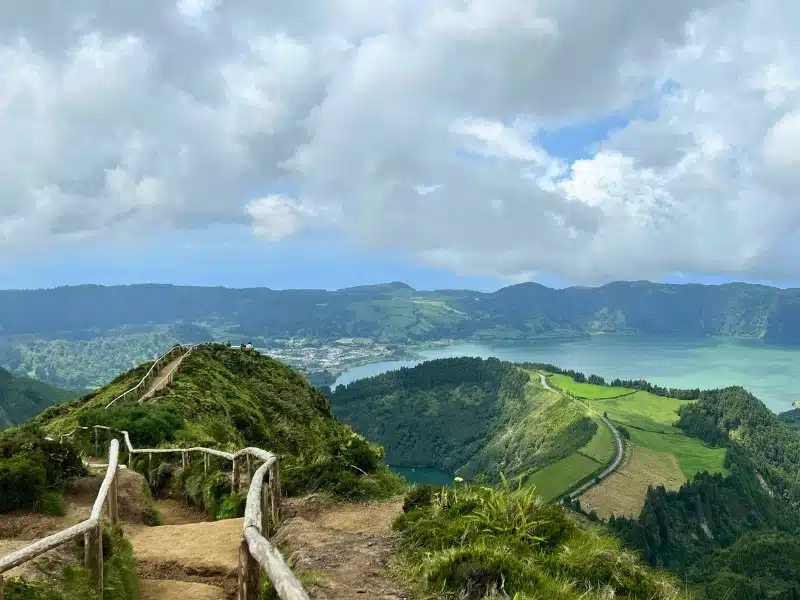 path with wooden handrailswith a view of lush fields and woods to a turquoise bay