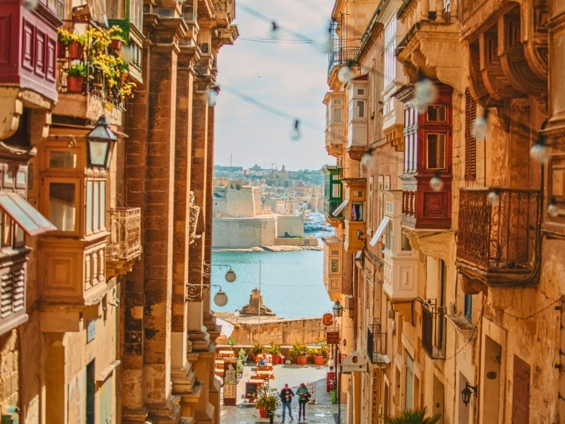 Tall townhouses with ornate balconies and windows leading doen the the sea and a defensive fortress