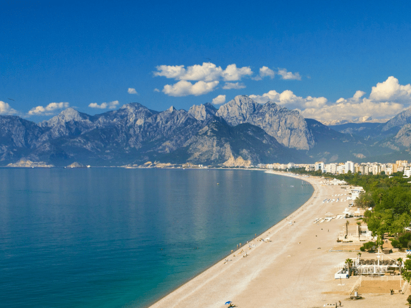 Long stetch of sandy beach backed by a town of white buildings with mountains in the distance