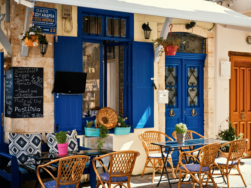 Restaurant with blue shutters and outside tables with a menu board advertising breakfast