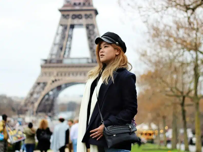Woman in Paris France dressed in a dark coat and cap with a cream scarf with the Eiffel tower in the background