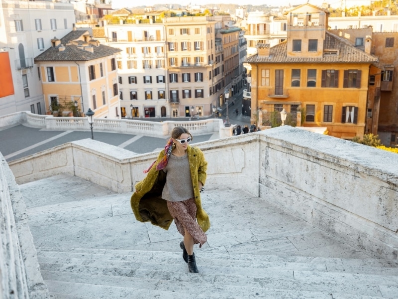 Sylishly dressed woman in Rome in fall running up stone steps