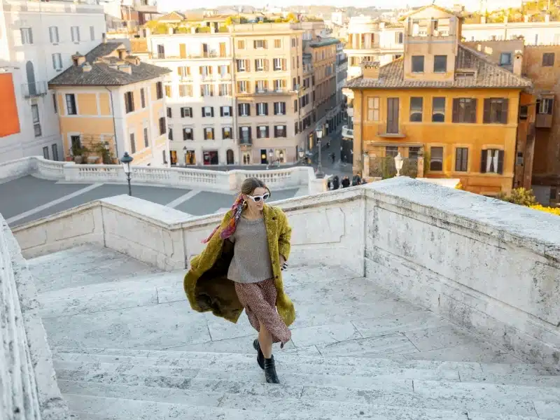 Sylishly dressed woman in Rome in fall running up stone steps