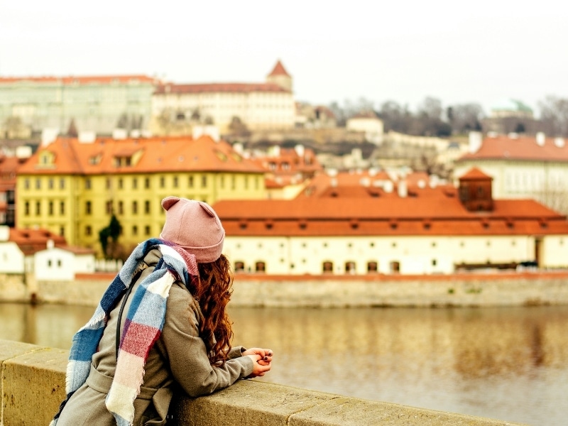 Woman wearing a colourful hat and scarf leaning on a bridge in Prague, Czech Republic 