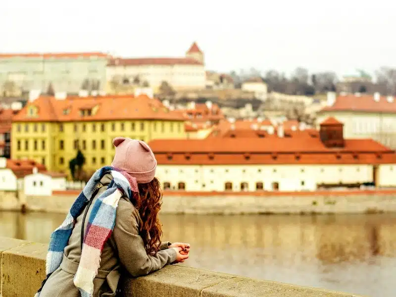 Woman wearing a colourful hat and scarf leaning on a bridge in Prague, Czech Republic 