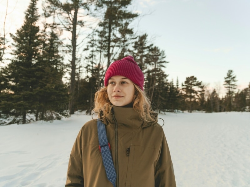 Woman wearing red woollen hat and khaki cold weather coat in a snowy environment