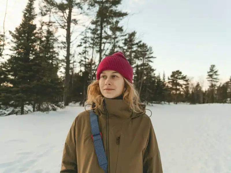 Woman wearing red woollen hat and khaki cold weather coat in a snowy environment
