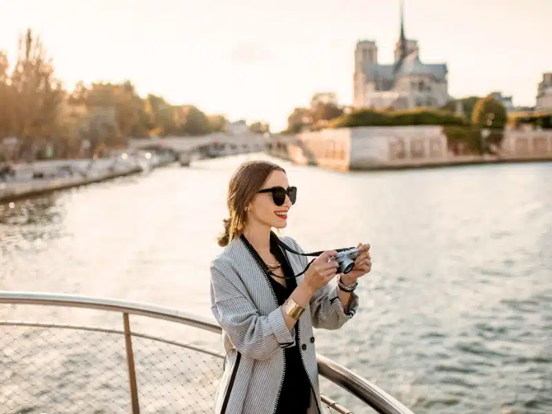 Stylish woman wearing a blazer and sunglasses on a boat in Paris France with Notre Dame in the background