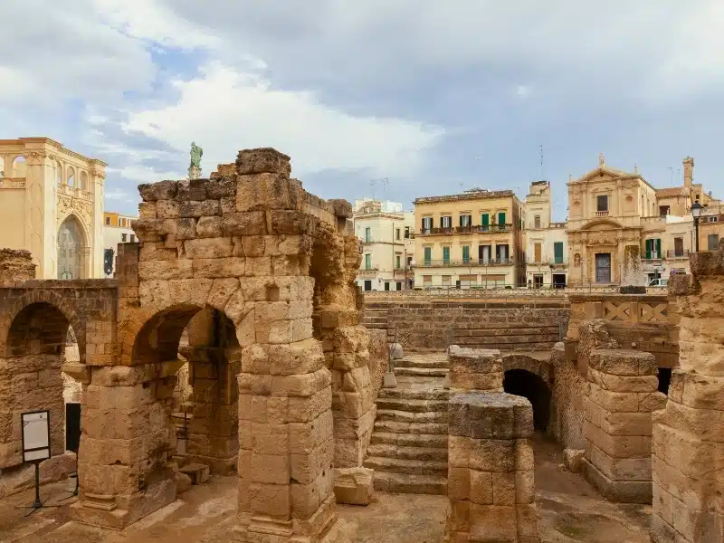 An aerial shot of historic exterior buildings with ancient stone arch gates with blue sky in Lecce, Italy