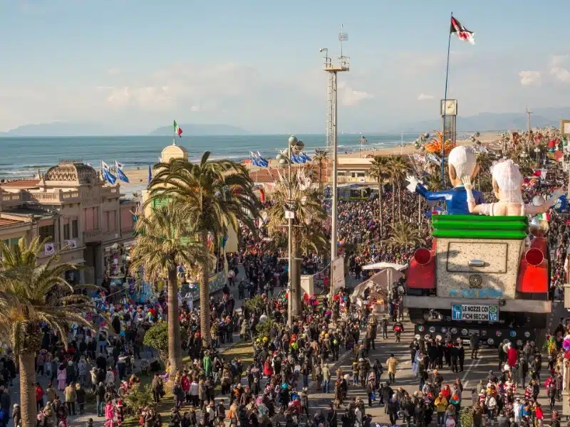 street by the beach lined with palm trees and many people attending an Italian Carnival