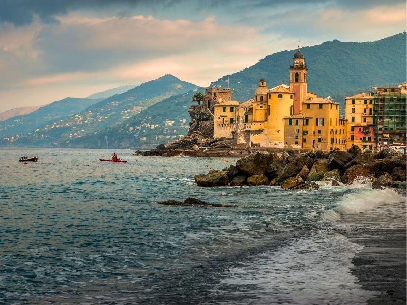 The picturesque coast with turquoise waves Mediterranean sea and colorful houses, tower of church against a backdrop of mountains at Camogli, Ligure, Italy.