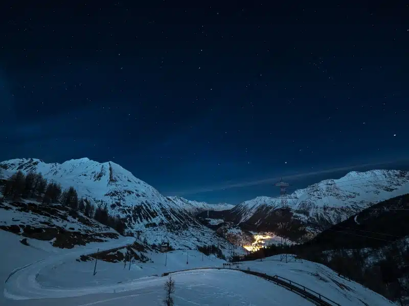 Aerial view of a town glowing in the night in Aosta Valley, Italy with starry sky and majestic mountain landscape illuminated by the moon