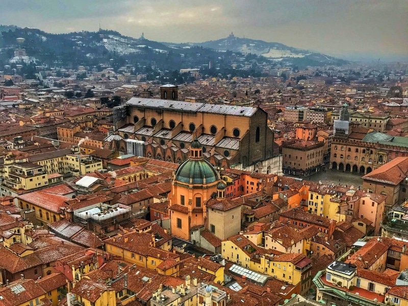 Bird's eye view of a wet Bologna Italy during daytime with snow dusted mountains in the distance