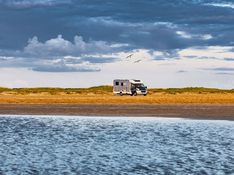 silver and white motorhome parked by low grassy dunes by the sea
