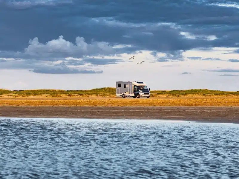 silver and white motorhome parked by low grassy dunes by the sea