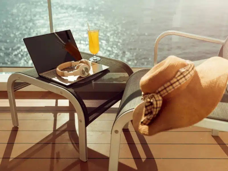 Ocean view balcony terrace on a cruise ship with laptop and headphones arranged on rattan stool with morning light 