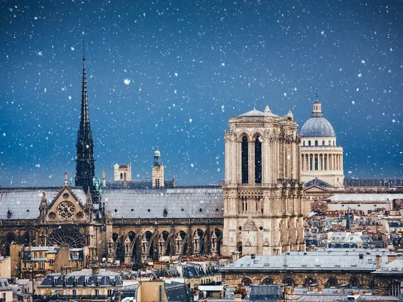 Historic Parisian buildings with domes and spires on a dark night in the snow