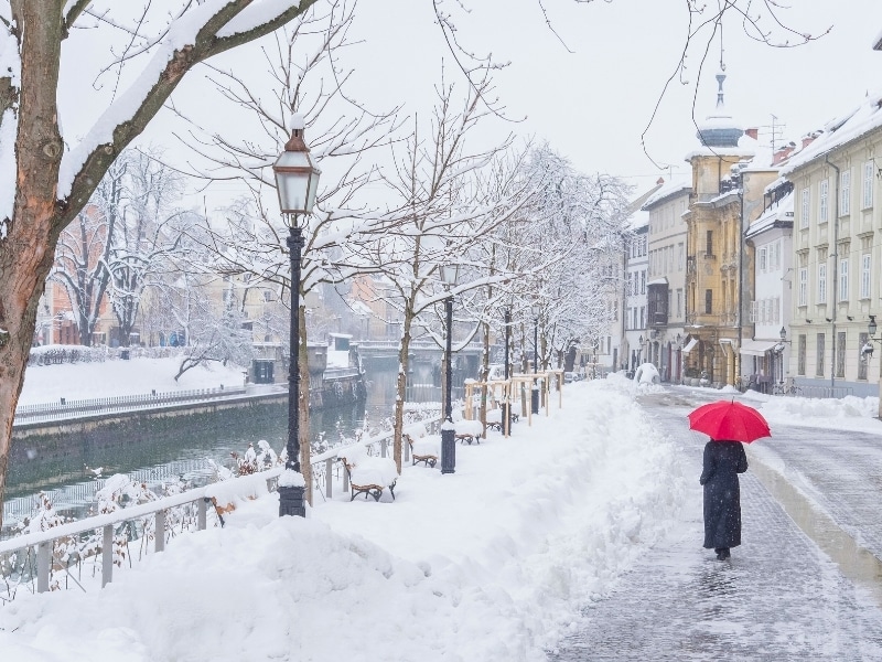 Woman with red umbrella walking in snowy day on empty street of Ljubljana