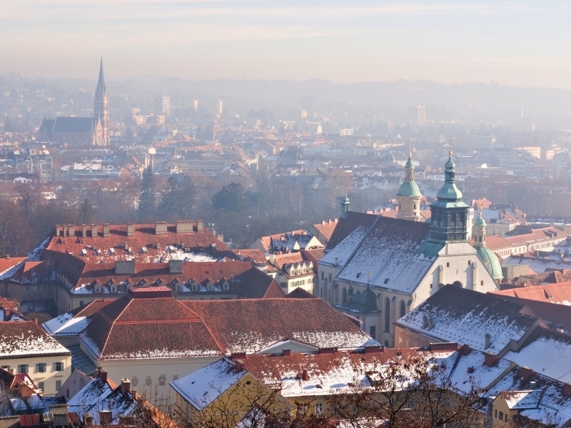 View of rooftops and chrch spires dusted with snow in Graz, Austria