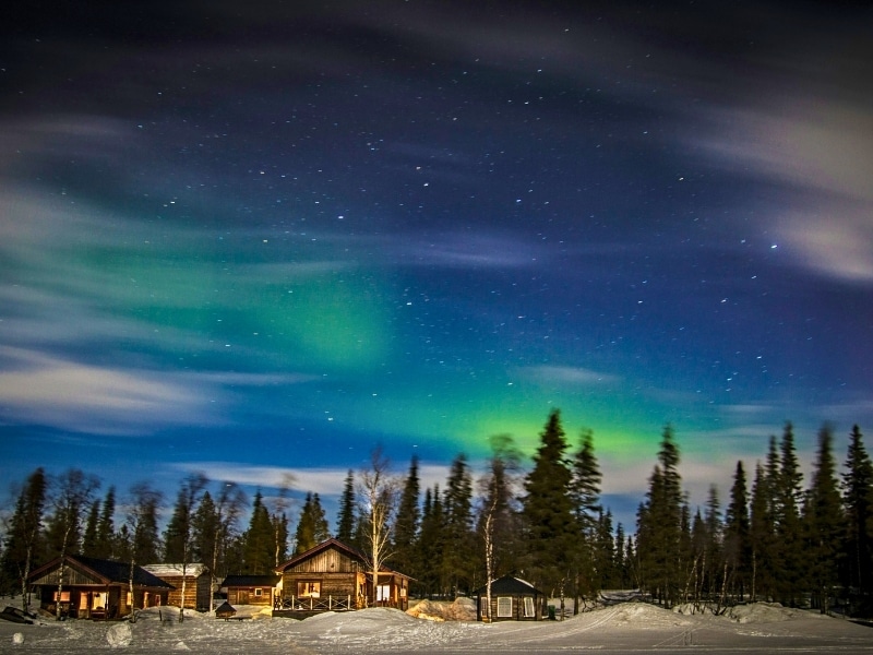 Northern lights in a starry sky over wooden huts in a snowy forest in Kiruna, Sweden
