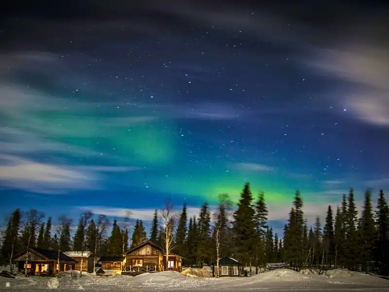 Northern lights in a starry sky over wooden huts in a snowy forest in Kiruna, Sweden