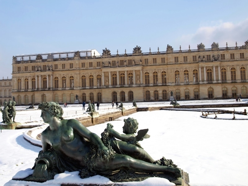 Garden sculptures and pond in front of the royal residence at Versailles near Paris in France in winter scenery, the snow