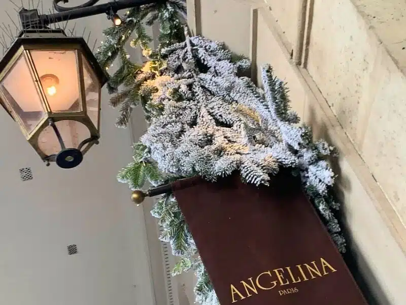 Brown flag sign for "Angelina Paris" with an old-fashioned light and Christmas fir decorations
