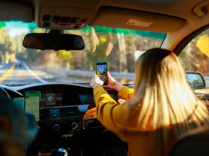 Female passenger in a car with a phone in her hand taking an image through the windscreen