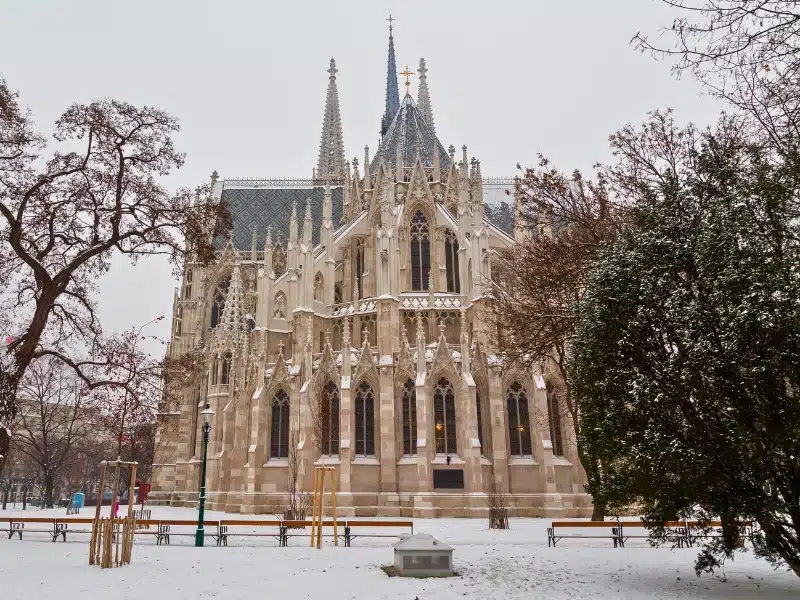 The outside of the Votive Church in Vienna during the day in the winter. Snow can be seen.